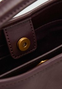 Intérieur d'un sac à main en cuir bourgogne foncé avec une fermeture à bouton-pression en métal doré et des détails de couture soignés le long des bords.