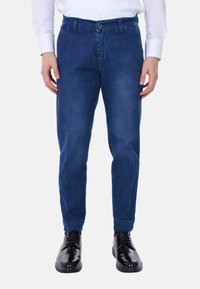 Pantaloni in denim blu con una vestibilità affusolata, dotati di chiusura a pulsante e tasche laterali. Abbinati a eleganti scarpe nere lucide.