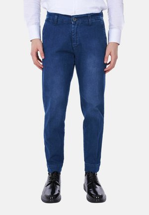 Pantaloni in denim blu con una vestibilità affusolata, dotati di chiusura a pulsante e tasche laterali. Abbinati a eleganti scarpe nere lucide.