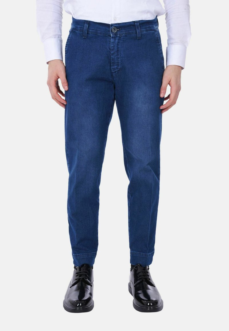 Pantaloni in denim blu con una vestibilità affusolata, dotati di chiusura a pulsante e tasche laterali. Abbinati a eleganti scarpe nere lucide.