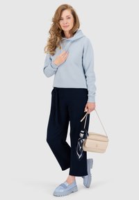 Felpa azzurra chiara, pantaloni blu navy a gamba larga e scarpe azzurre pastello. Borsa beige con una sciarpa decorativa. Materiali morbidi e vestibilità casual.