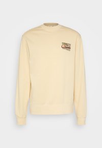 Sudadera color crema con cuello redondo y mangas largas. Presenta un parche bordado con un diseño de montaña y sol en el pecho.