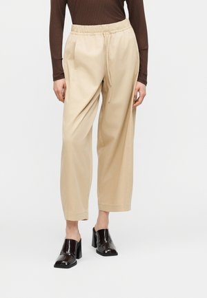 Μπεζ φαρδιά παντελόνια με ελαστική μέση και κορδόνι, συνδυασμένα με καφέ μακρυμάνικη μπλούζα και μαύρα μπαλαρίνια με τετράγωνη μύτη και τακούνι.