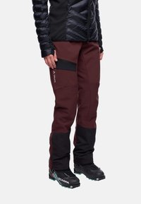 Smaragdrode outdoorbroek met zwarte accenten en zijrits zak. Gemaakt van duurzaam, weerbestendig materiaal. Gecombineerd met zwarte laarzen.