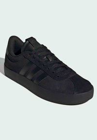 Crne atletske cipele s gornjim dijelom od suviše, okruglim vrhom, teksturiranim vezicama, tri pruge sa strane i ravnim gumenenim potplatom.