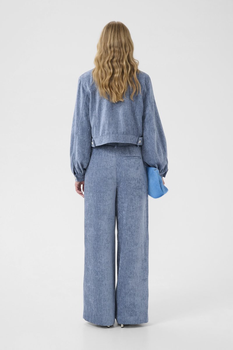 Light blue denim jacket with puff sleeves, paired with matching wide-leg trousers, holding a blue clutch. Textured fabric with subtle pattern.