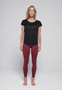 Zwart kortmouwig sporttop gecombineerd met bordeauxrode leggings met rode accentnaden, een gladde textuur en een aansluitend ontwerp.