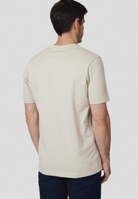 Beżowa bawełniana koszulka z krótkim rękawem i okrągłym dekoltem. Charakteryzuje się prostym wzornictwem, prostym dołem i małym logo w pobliżu kołnierza.