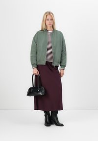 Zelen bomber jakna z ribastimi manšetami, prugasta majica, burgundska maxi krila, črna torbica in črne škornje do kolen. Gladke teksture in slojevito oblačenje.