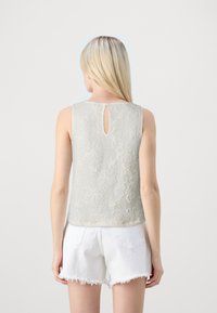 Top sin mangas de un gris claro con textura floral y detalle de ojal en la espalda, hecho de una tela suave. Combinado con pantalones cortos blancos deshilachados.