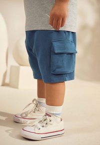 Blue cargo shorts made from soft fabric, featuring a side pocket. Paired with white sneakers and light socks. Simple design and neutral colors.