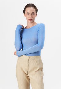 Himmelblaues Langarmshirt mit Rundhalsausschnitt und Daumenlöchern, kombiniert mit beigen, strukturierten Hosen. Weicher, eng anliegender Stoff.