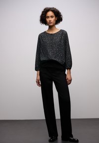 Blusa nera a maniche lunghe con riquadratura abbottonata, caratterizzata da un motivo a pois discreto e una vestibilità comoda, abbinata a pantaloni neri a gamba larga.