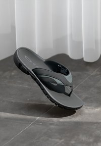 Sandalia de dedo negra con parte superior texturizada, plantilla suave y suela duradera. Diseño elegante con un mínimo de marca en la plantilla.