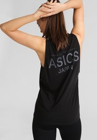 Černá bezrukávová sportovní tílko s kulatým výstřihem, volným střihem a výrazným logem ASICS na zadní straně. Lehce a hladce tkaná látka.