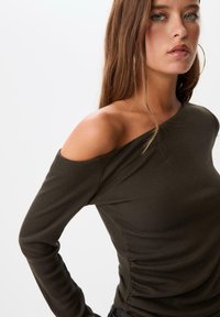 Oliven grøn ribbet langærmet top med off-shoulder design, der har struktureret stof og en tætsiddende pasform. Diskret rynkning i siden.