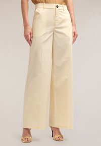 Crème wijdgesneden broeken van soepele stof met een knoopsluiting, voorzien van zijzakken en een getailleerde pasvorm.