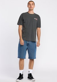 T-shirt en coton gris à manches courtes, associé à un short en denim bleu qui arrive juste au-dessus des genoux, porté avec des baskets montantes noires.
