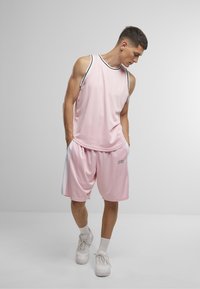 Débardeur de sport rose avec accents noirs et shorts assortis. Les shorts présentent des panneaux latéraux et le logo "DEF". Baskets blanches. Texture lisse.