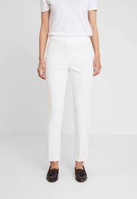 Witte op maat gemaakte broek met een slanke pasvorm, met een gladde textuur en minimale naden, gecombineerd met donkere loafers voor contrast.