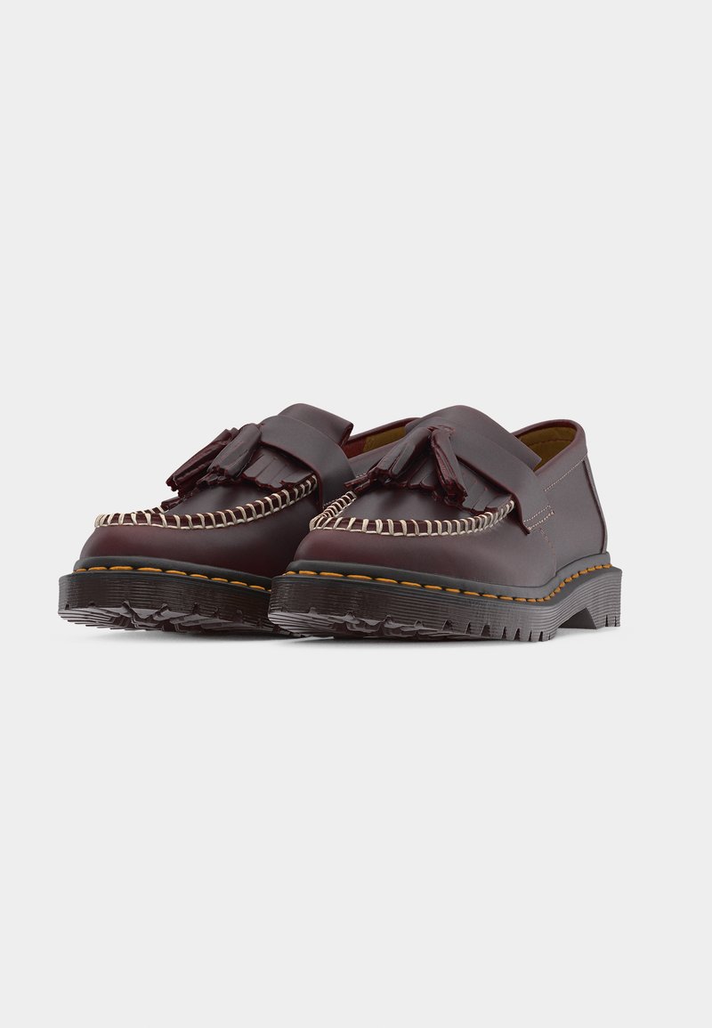 Mocassini in pelle marrone scuro con nappine, suole nere spesse e zigrinate e cuciture bianche a contrasto lungo il bordo anteriore.