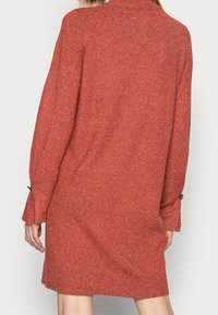 Långärmad klänning i texturerad rostfärgad stickning, med hög halsringning och knappdetaljer vid ärmsluten. En enkel, avslappnad passform.