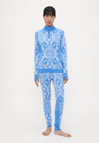 Blue patterned loungewear set with a zip-up top and fitted pants. Features geometric designs in lighter shades and contrasting cuffs.