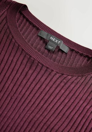 Bordeaux-rot gerippter Pullover mit Rundhalsausschnitt; das Etikett zeigt "NEXT" und "HERGESTELLT IN CHINA." Der Stoff hat eine strukturierte Optik mit vertikalen Streifen.