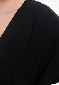 Schwarzes V-Ausschnitt-Oberteil aus weichem, leichtem Stoff, mit lockerem Schnitt und drapierten Schultern. Glatte Textur mit minimalen Details.