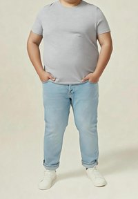 Camiseta gris de manga corta combinada con jeans de color azul claro y zapatillas blancas. Los jeans están doblados en los puños, creando un look casual.