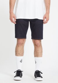 Donkerdenim shorts met contraststiksels, een regular fit, gecombineerd met zwarte lage sneakers en witte gestreepte sokken.