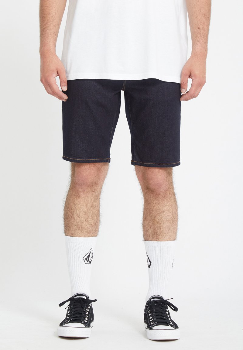 Donkerdenim shorts met contraststiksels, een regular fit, gecombineerd met zwarte lage sneakers en witte gestreepte sokken.