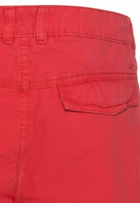 Shorts en coton rouge avec une poche arrière, des coutures apparentes et une texture lisse. La ceinture est faite du même matériau.