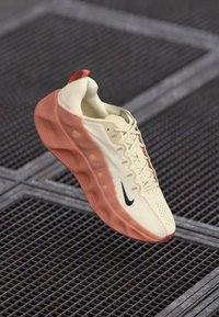 Nike sneaker in cream with an orange sole, featuring a breathable mesh upper, textured detailing, and a black swoosh logo on the side.