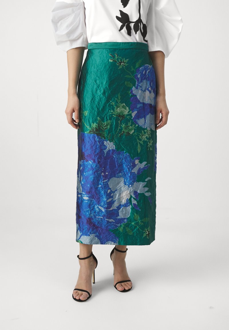Grön blommig maxikjol med ett abstrakt mönster av blå och ljusgrå blommor, texturerad tyg och en åtsittande midja. Svarta högklackade sandaler.