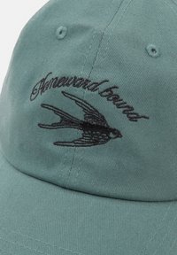 Green cotton cap with a structured design. Features black embroidered swallow logo and text "Homeward Bound" on the front.