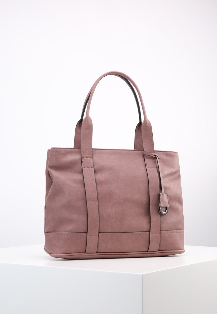 Sac fourre-tout en cuir mauve avec double bandoulière, forme rectangulaire et petite étiquette décorative suspendue à une des anses sur un piédestal blanc.