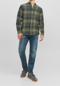 Grünes und marineblaues kariertes Flanellhemd mit Knopfleiste, langen Ärmeln und Brusttasche, kombiniert mit ausgewaschenen blauen Jeans und grauen Turnschuhen.