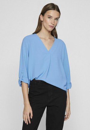 Lichtblauw V-hals top met driekwart mouwen, voorzien van opgerolde manchetten en een relaxed fit, gecombineerd met zwarte broek. Glad stof oppervlak.