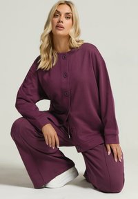 Lila lounge-set bestående av en knapp-up, oversized topp med långa ärmar och matchande vida byxor, tillverkad av mjukt, strukturerat tyg.