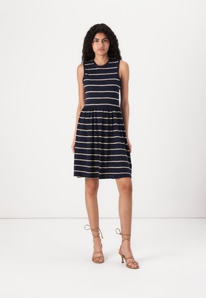 Rochie bleumarin cu dungi orizontale crem, design fără mâneci, parte superioară ajustată și fustă evazată. Purțată cu sandale cu toc înalt, de culoare bej, cu bretele.