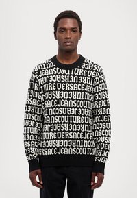 Maglione nero in maglia con un audace motivo testuale bianco ripetuto. Ha un collo tondo e polsini a coste, aggiungendo texture e dettagli.