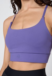 Fioletowy sportowy biustonosz z kwadratowym dekoltem, cienkimi ramiączkami i wytłoczonym logo na pasku. Wykonany z gładkiego, elastycznego materiału.