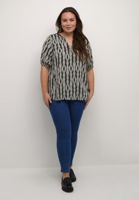 Blouse à manches courtes noire et beige à motif avec un col en V, associée à un jean skinny bleu et des mocassins noirs. Tissu lisse avec une coupe décontractée.