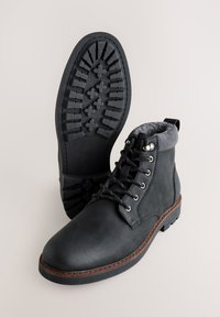 Ghete negre din piele cu manșetă gri de fleece, design cu șireturi, talpă de cauciuc cu relief texturat și cusături în contrast pe bază.