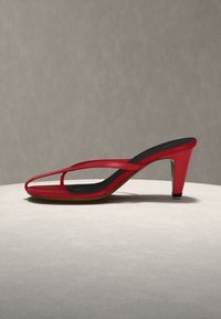 Κόκκινο σανδάλι με ψηλή λεπτή σόλα, λεπτά λουριά, μαύρη εσωτερική σόλα και μεσαίου ύψους λεπτό τακούνι πάνω σε φωτεινή επιφάνεια με ουδέτερο φόντο.