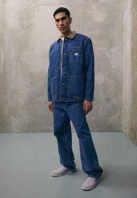 Denimjack met een lichtbruine corduroy kraag, twee voorzakken, gecombineerd met bijpassende denim jeans en paarse geruite instappers.