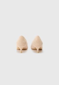 Zapatos de tacón alto de ante en color nude, con punta afilada y tacón fino. Presentan una textura suave y un diseño minimalista.