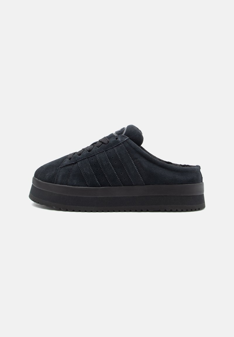 Čierne semišové slip-on topánky s okrúhlou špičkou, hrubou čiernou podrážkou a tromi horizontálnymi pruhmi na bočnej strane. Mäkka textúra, vyzdvihnutý dizajn.