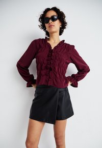 Μαρούλι μπλούζα με ρίγες και μακριά μανίκια, συνδυασμένη με μαύρες κοντές σατέν δερμάτινες σορτς με σχέδιο τύπου τύλιγμα και τσέπες.